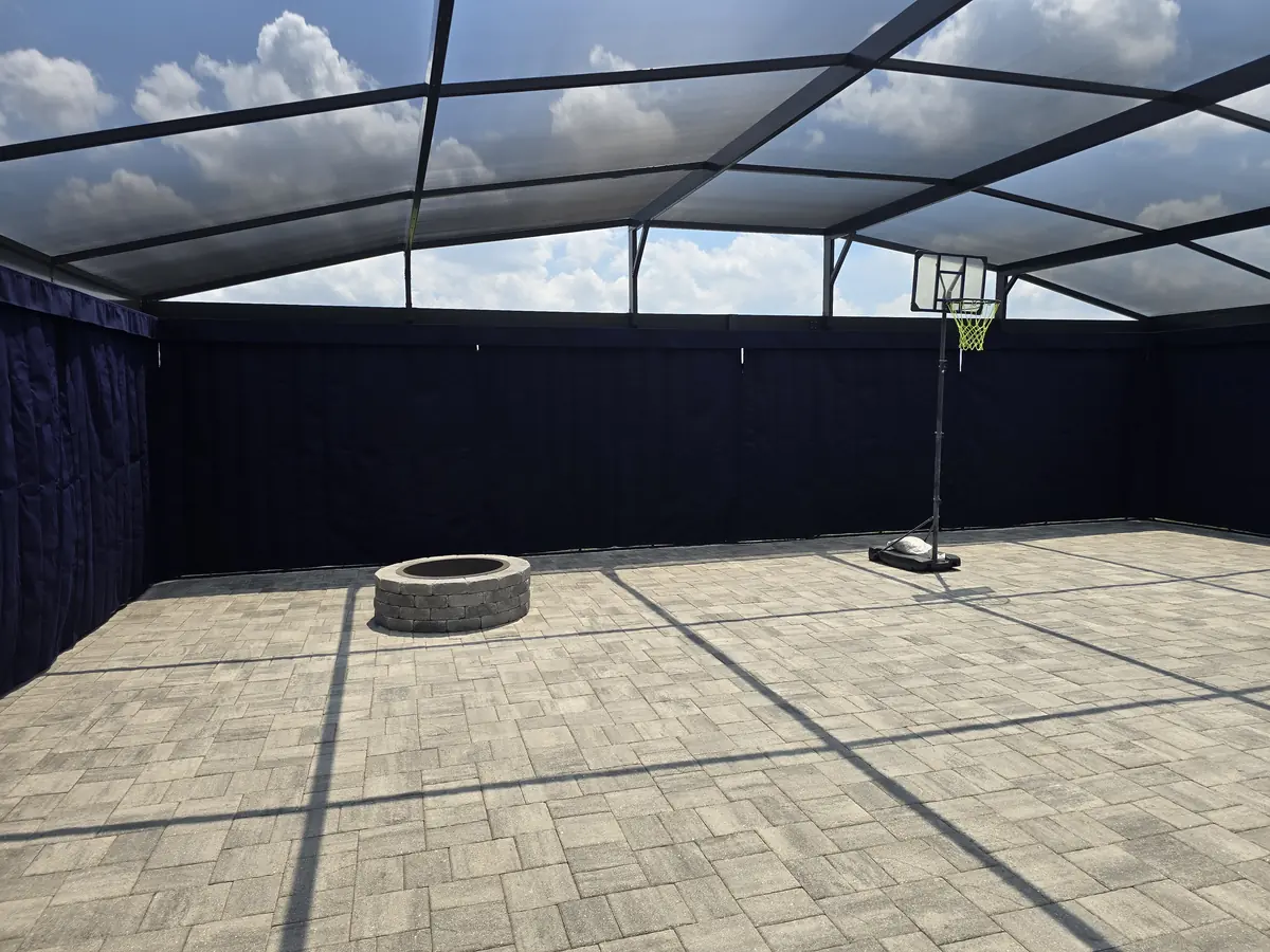 Black privacy curtains wrapping a paver patio with a fire pit inside a screen enclosure