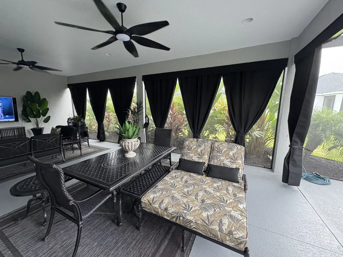 Black privacy curtains tied back around a lanai dining area with a hot tub
