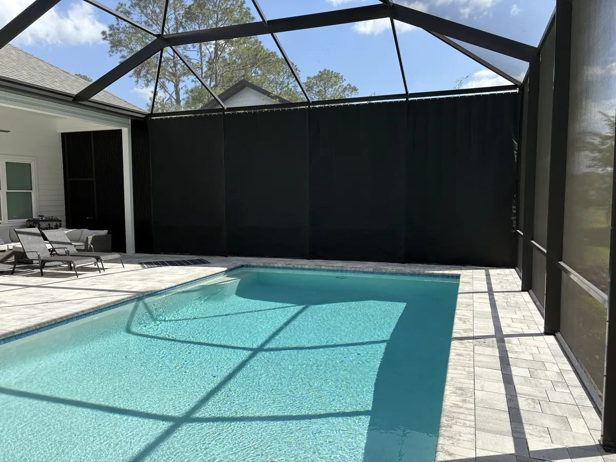 Black privacy curtains along one wall of a pool cage beside a rectangular pool