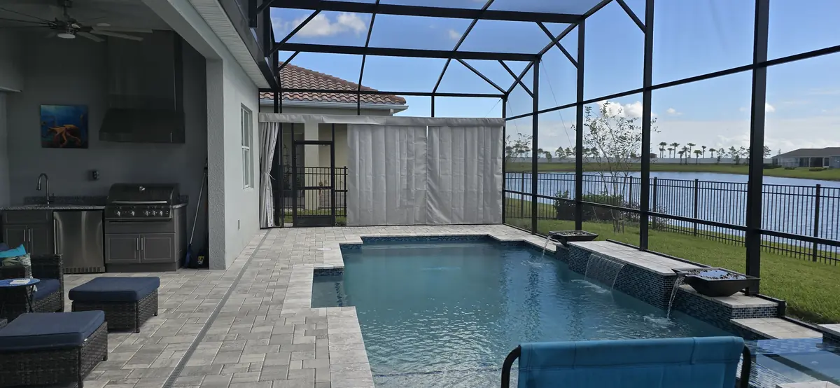 Cream privacy curtains along a lakefront pool and outdoor kitchen