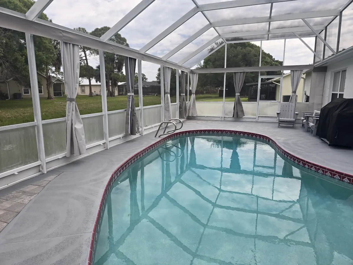 Wide view of gray tie-back privacy curtains around a pool in a white screen enclosure