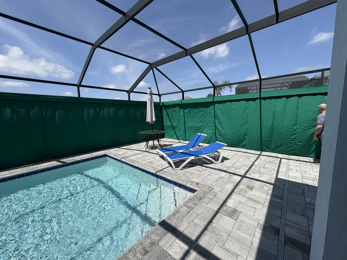 Dark green privacy curtains wrapping a pool cage with blue lounge chairs
