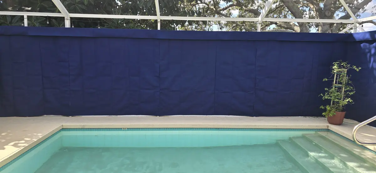 Navy privacy curtains along a pool cage wall beside a pool with blue chairs