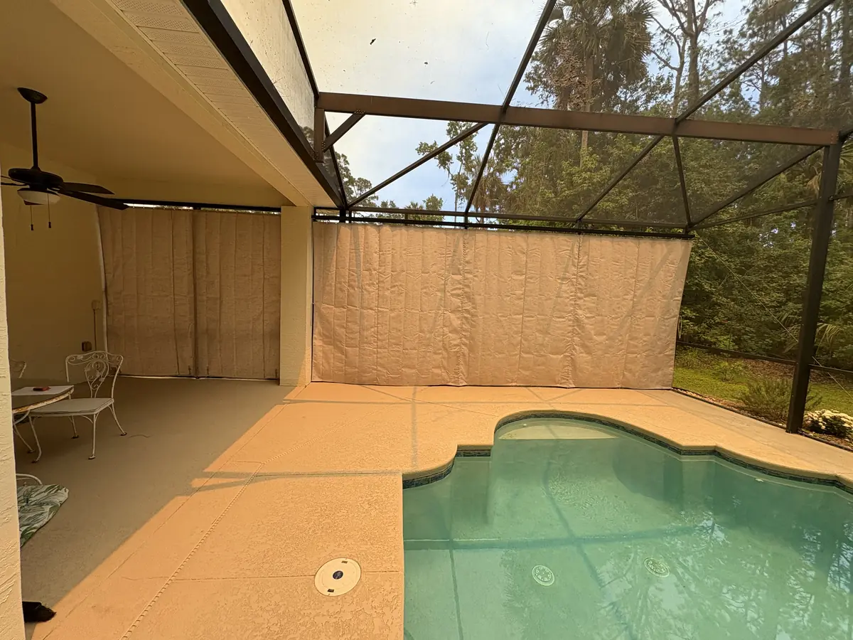 Tan privacy curtains on a covered lanai with a ceiling fan and pool