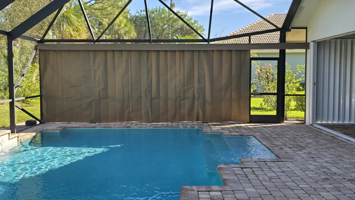 Tan privacy curtains on the back wall of a pool cage with a spa