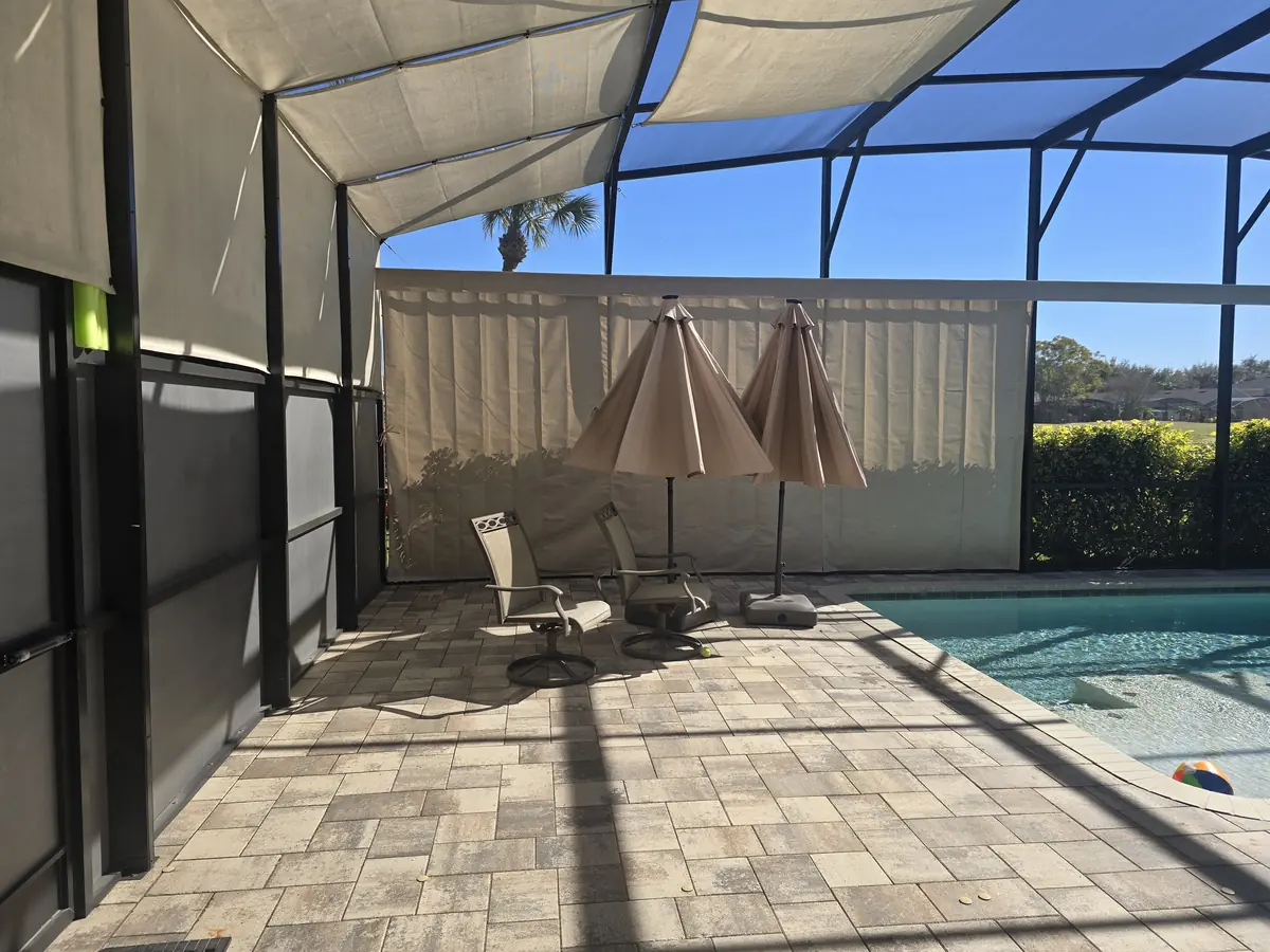 Tan privacy curtains behind patio umbrellas and a pool in a Florida lanai