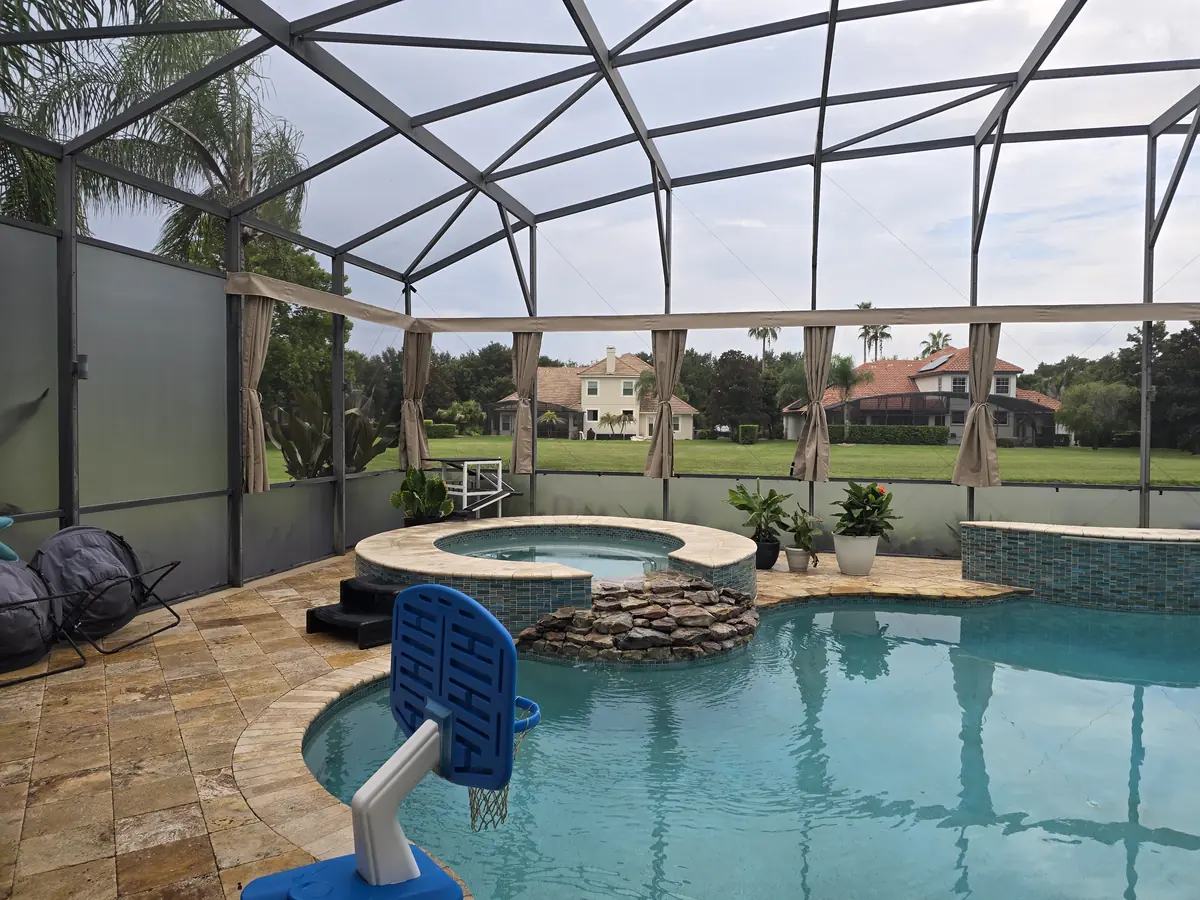 Tan tie-back privacy curtains around a pool and spa with a rock waterfall in Florida