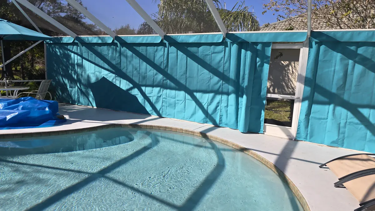 Teal privacy curtains wrapping a pool in a white screen enclosure