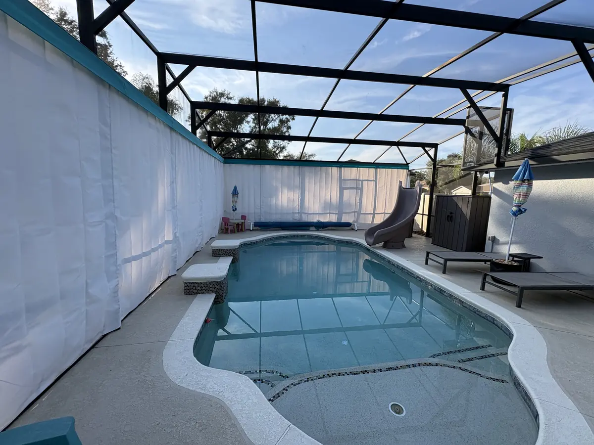 White privacy curtains around a family pool with a slide in a Florida pool cage