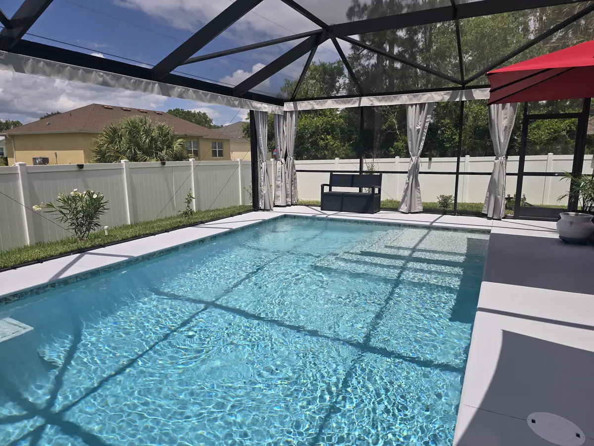 White privacy curtains tied back around a pool with a red umbrella in a Florida screen enclosure
