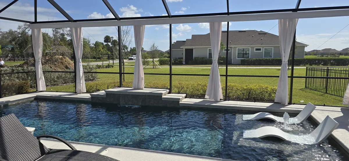 White tie-back privacy curtains around a pool with loungers and a lake view