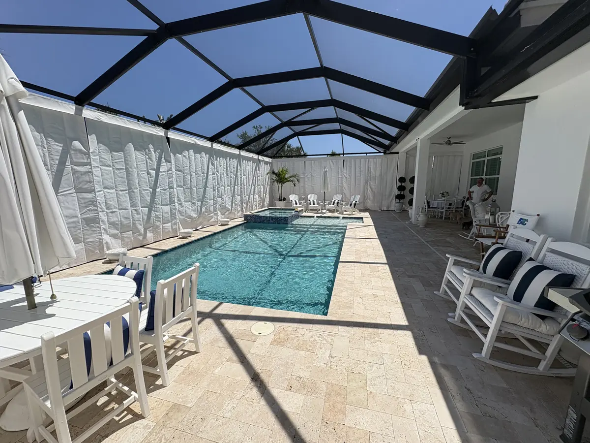 White tie-back privacy curtains around a pool with a white dining set on the deck