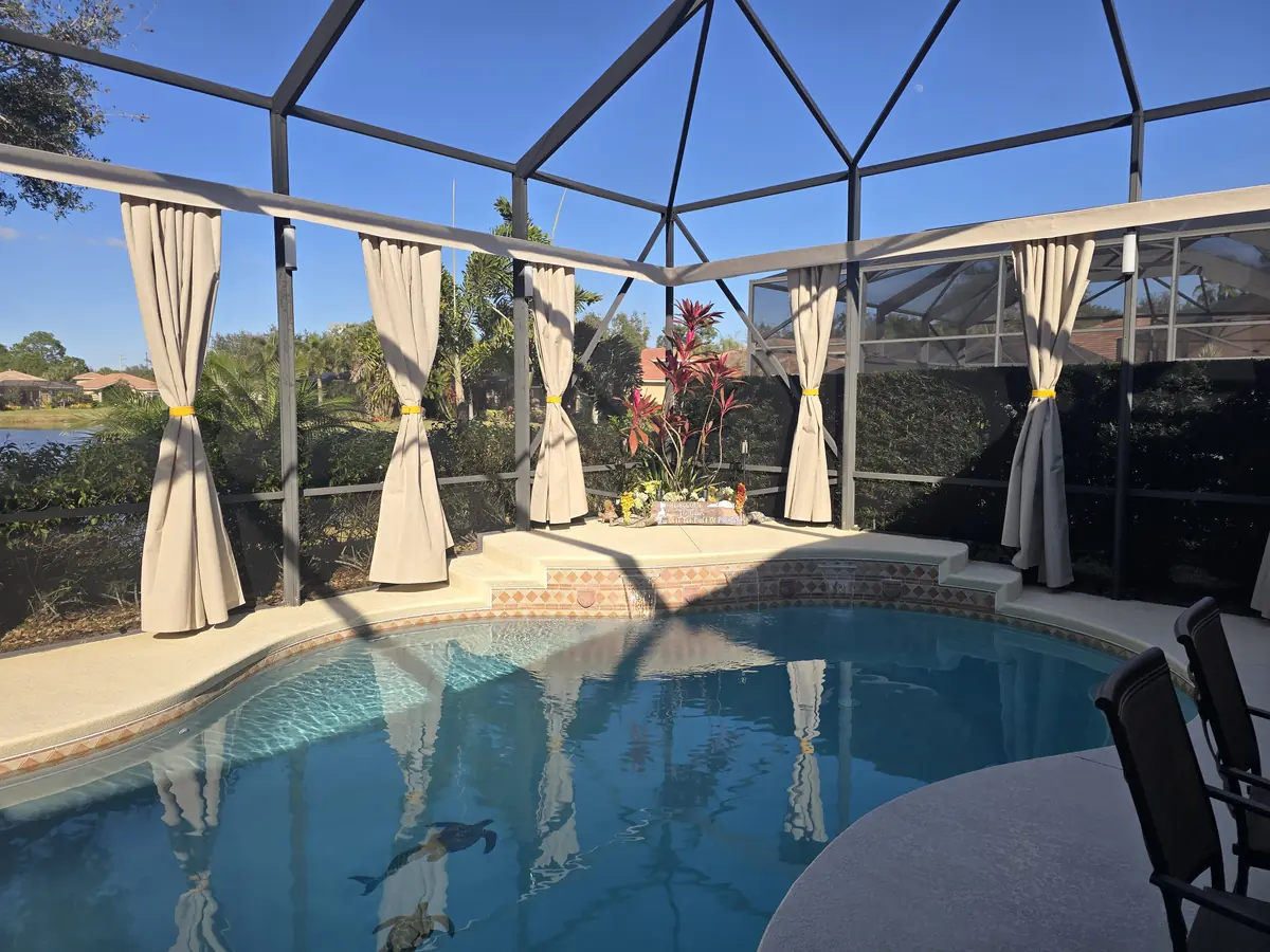 White tie-back privacy curtains around a pool with an umbrella and lounge seating