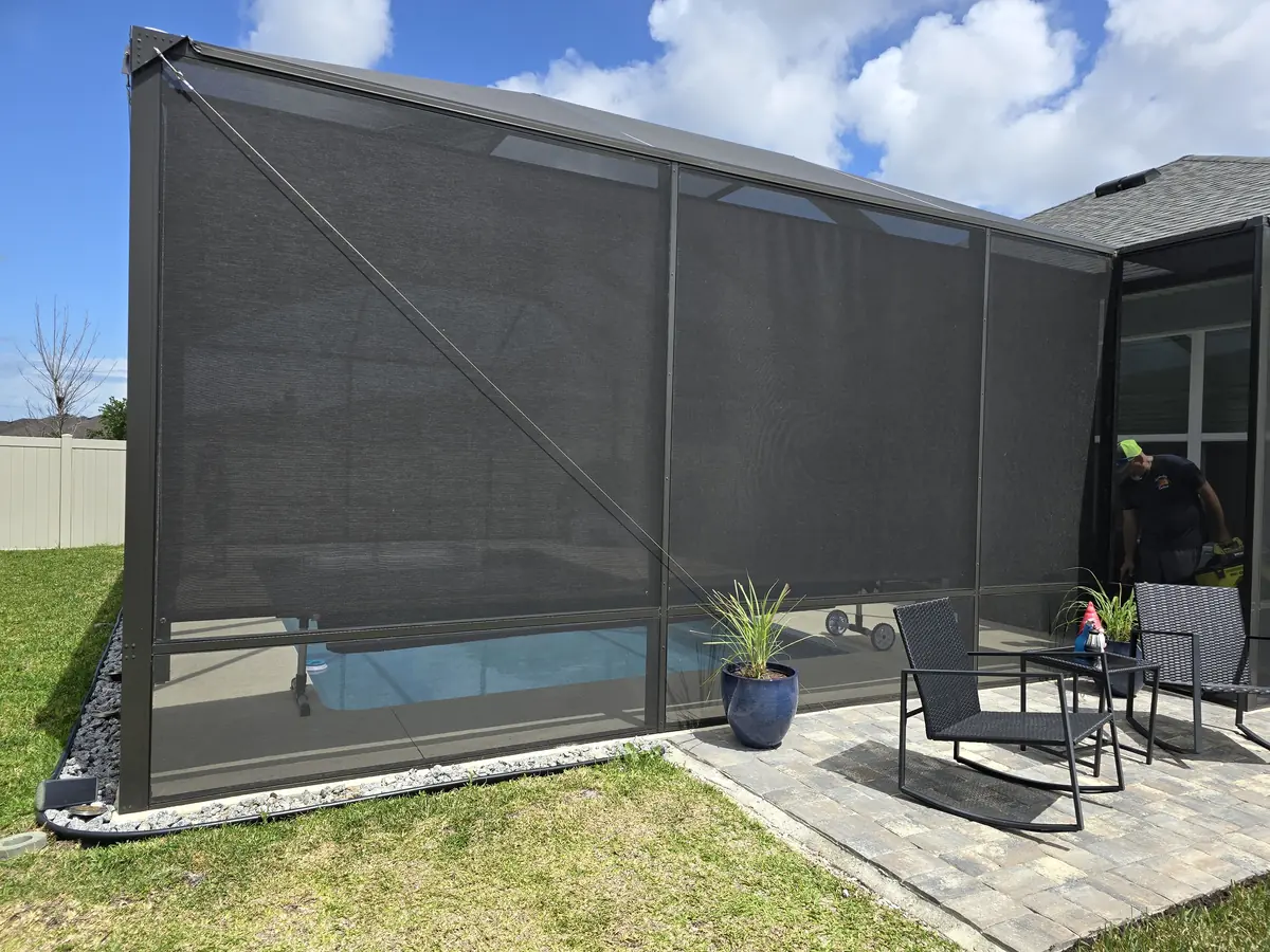 Charcoal roller shades seen from outside a Florida screen enclosure with patio seating