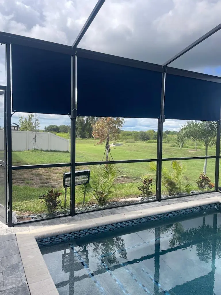 Cocoa brown roller shade lowered beside a pool in a bronze screen enclosure