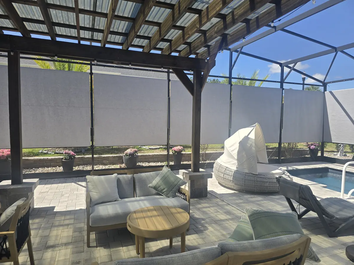 Gray roller shades behind a pergola seating area inside a pool enclosure
