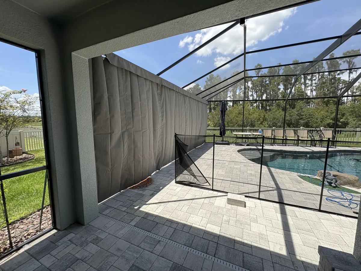 Gray roller shade lowered on a lanai overlooking a pool with a safety fence in Florida