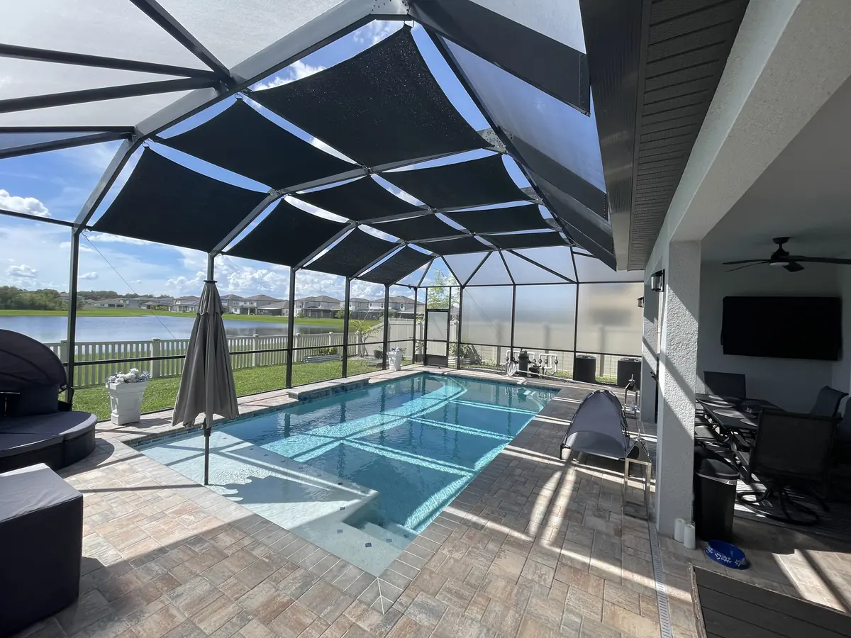 Black shade sails over a lakefront pool and lanai in a Florida screen enclosure