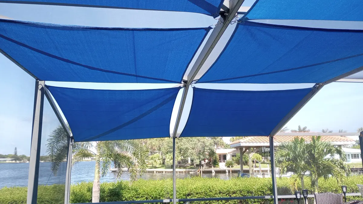 Blue shade sails over a lanai with a view of a canal and palm trees