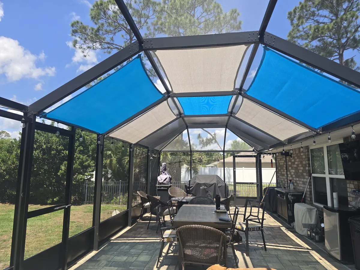Blue shade sails covering a lanai seating and dining area inside a pool enclosure