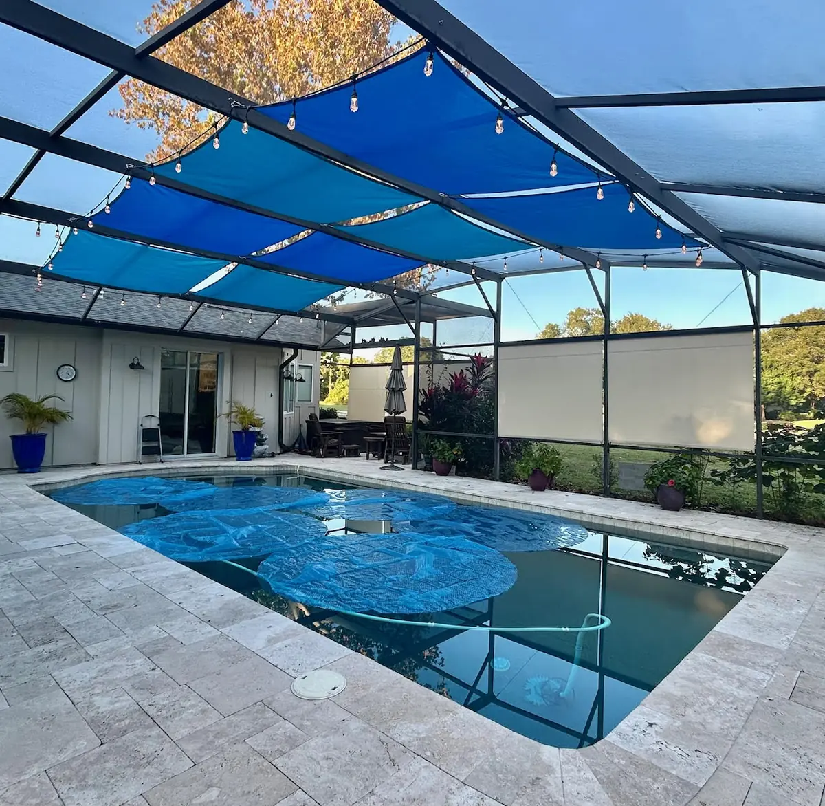 Blue shade sails over a pool at dusk with string lights in a Florida pool cage