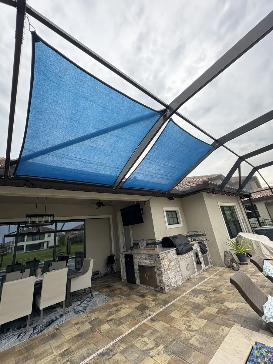 Blue shade sail over a covered lanai kitchen and pool in a bronze screen enclosure