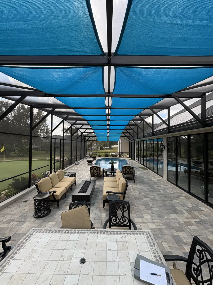 Blue shade sails over a lanai seating area with a sectional sofa and pool beyond