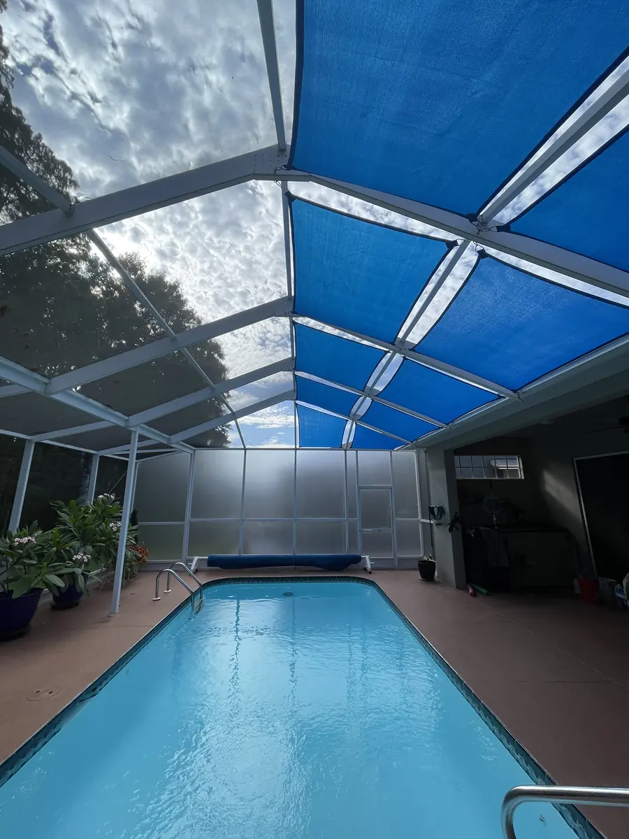 Blue shade sail running the length of a narrow pool in a Florida pool cage