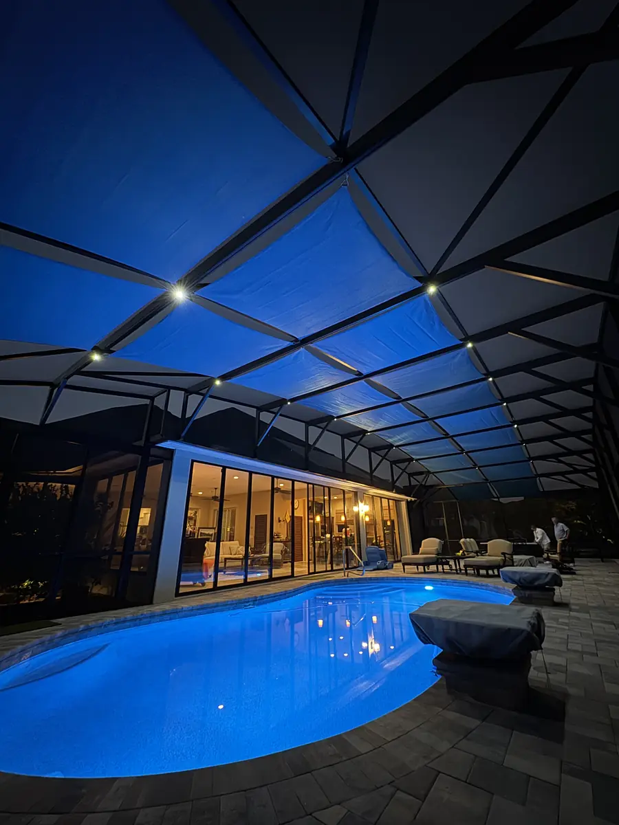 Blue shade sails lit from below at night over a Florida pool enclosure
