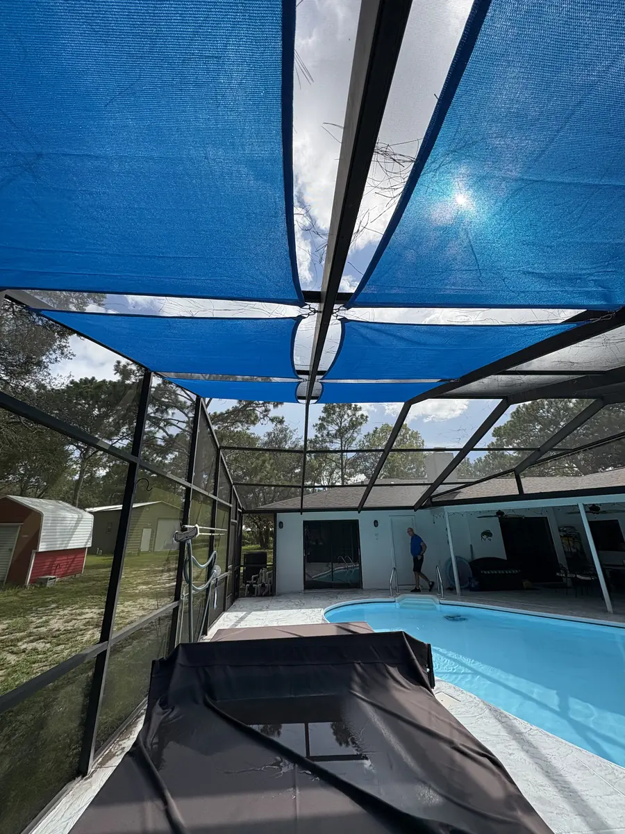 Blue shade sail stretched over a pool deck inside a Florida screen enclosure