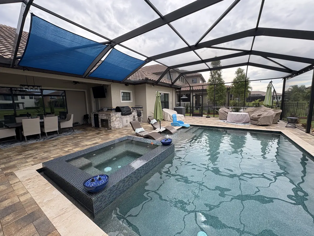 Blue shade sails installed over a pool and raised spa inside a Florida screen enclosure