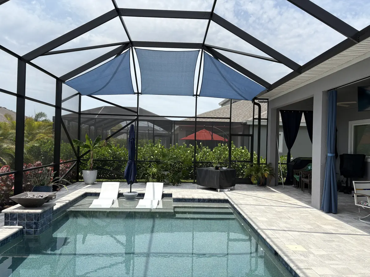 Blue shade sail over a pool and spa with a covered lanai in a bronze screen enclosure