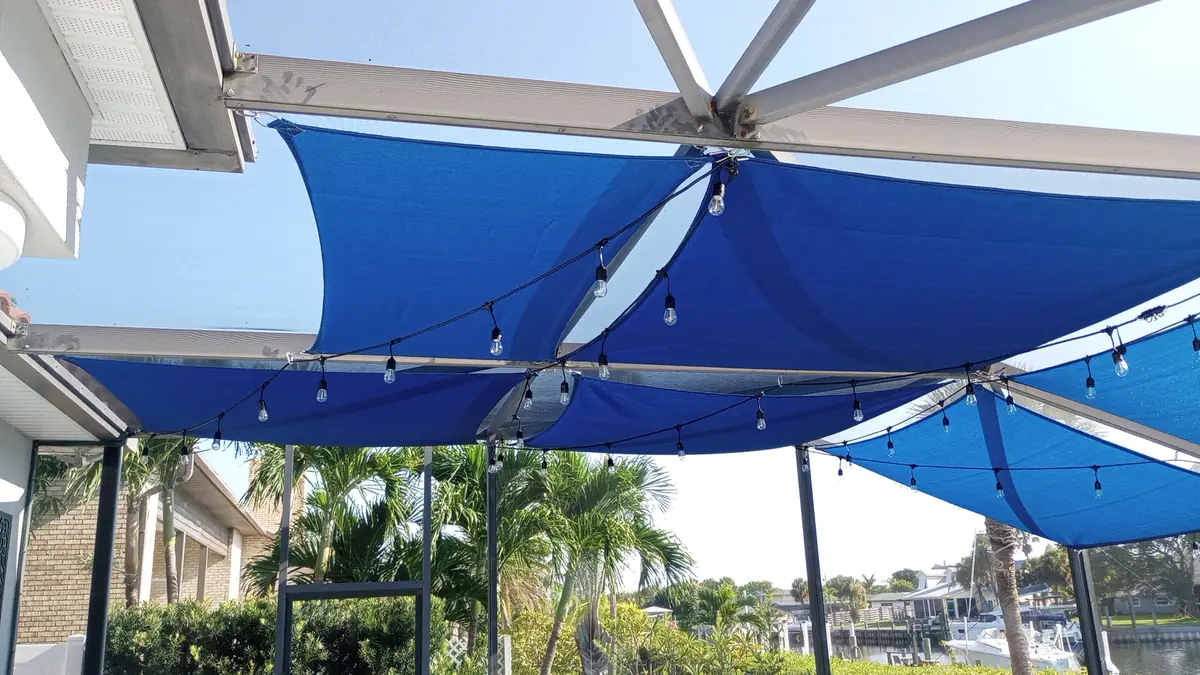 Blue shade sails and string lights over a waterfront lanai dining area