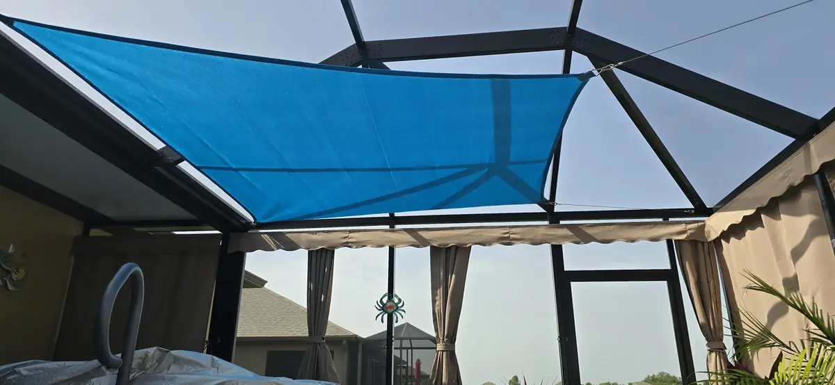 Blue shade sail overhead with tan privacy curtains along the lanai wall