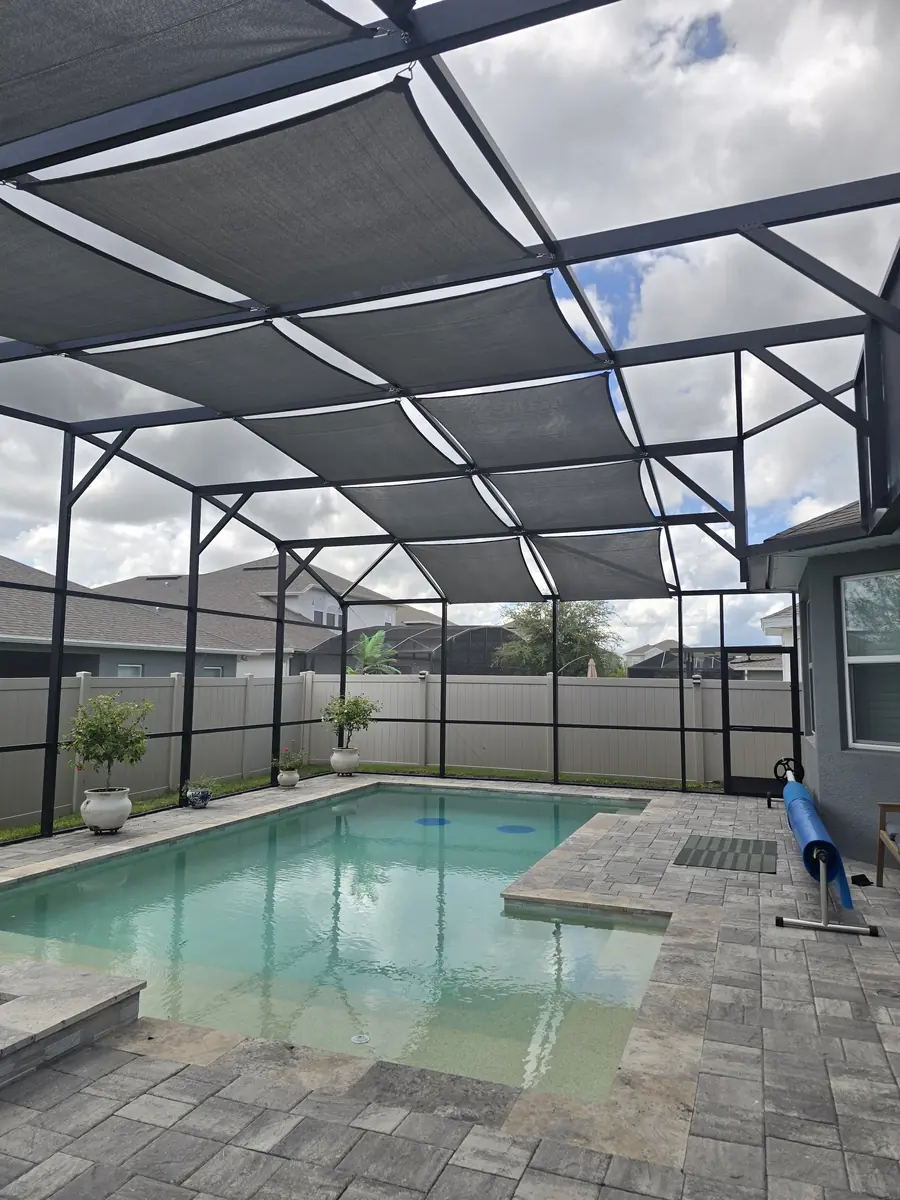 Charcoal gray shade sails over a pool in a bronze aluminum screen enclosure