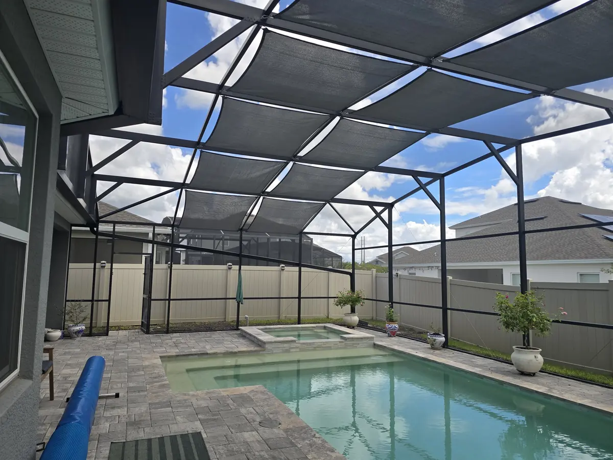 Wide view of charcoal shade sails over a pool in a bronze screen enclosure