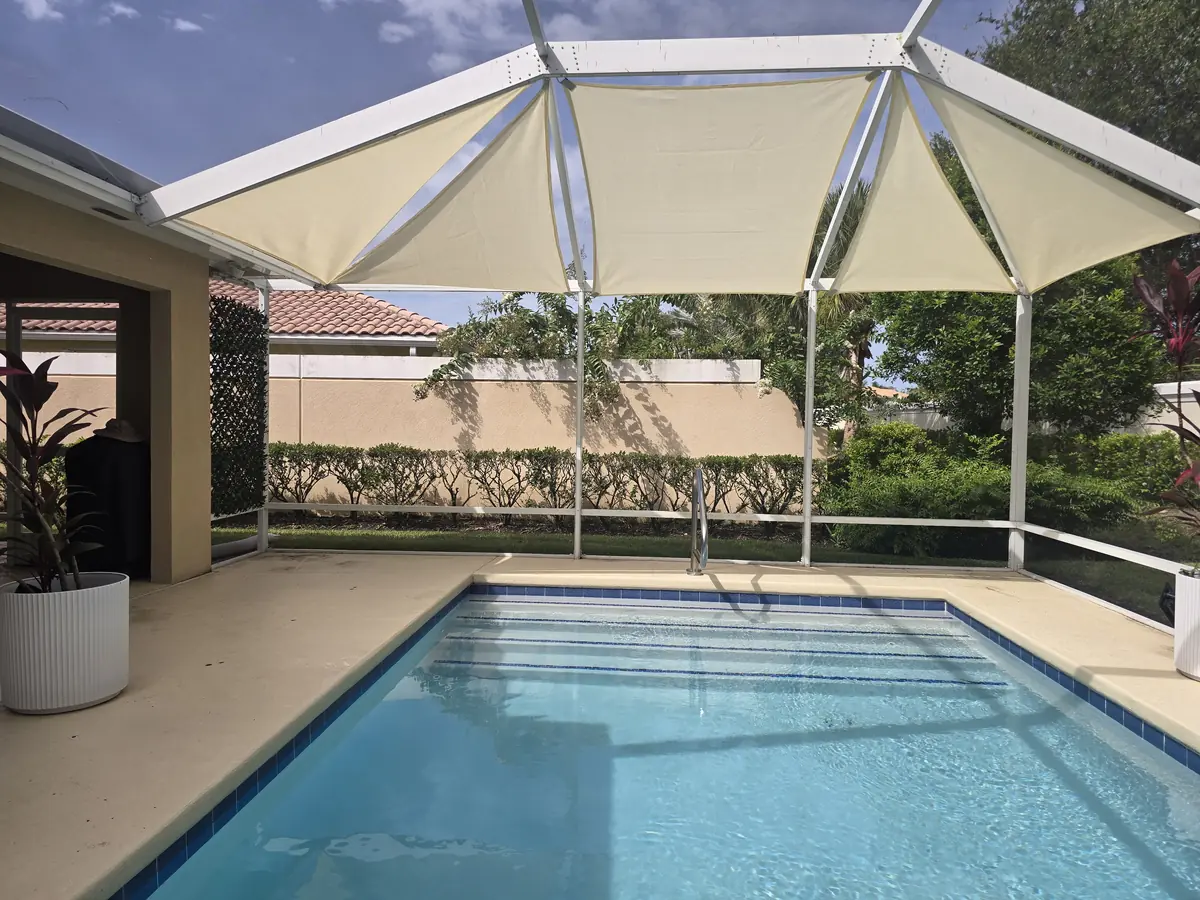 Cream shade sails over a rectangular pool in a white aluminum screen enclosure