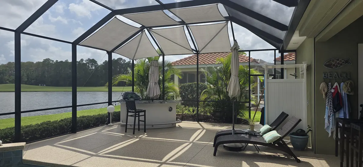 Gray shade sails over a lakefront lanai with lounge chairs and a pool