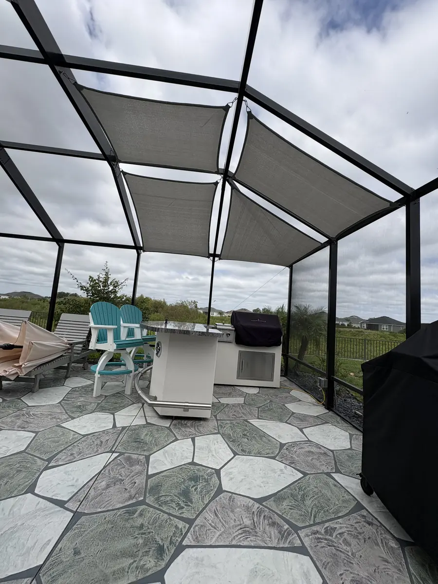 Gray shade sail over a patio bar with bar stools inside a screen enclosure