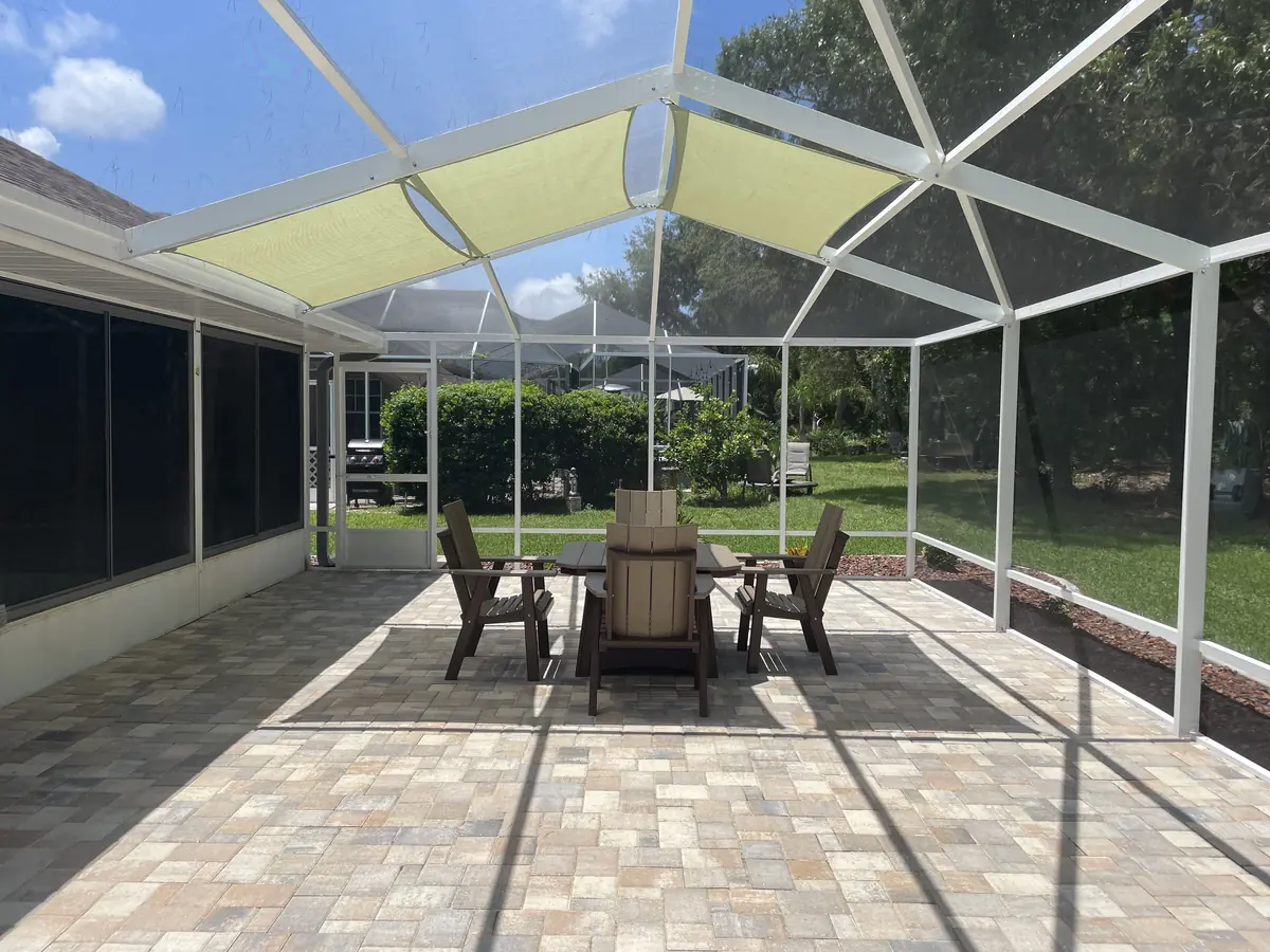Wide view of a lime green shade sail over a dining set in a white screen enclosure