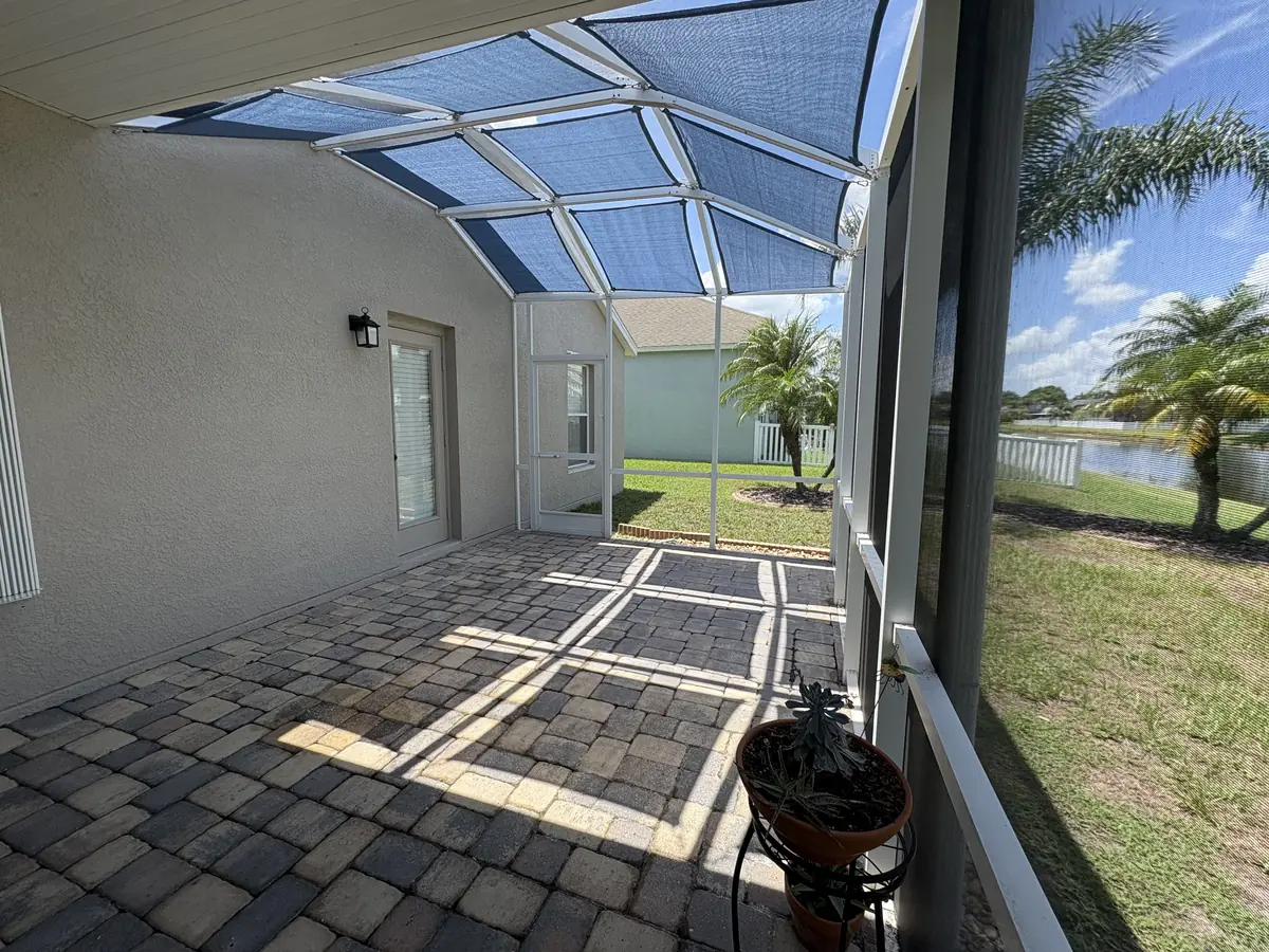 Light blue shade sails over a lanai with a lake and palm trees beyond the screen