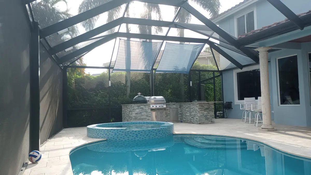 Light blue shade sails over a pool, spa, and outdoor kitchen in a Florida pool cage