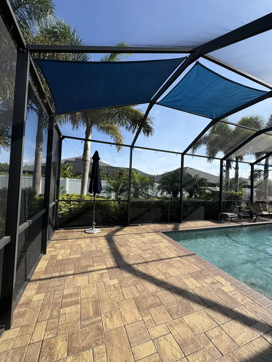 Navy blue shade sail over a paver pool deck with palm trees outside the screen enclosure