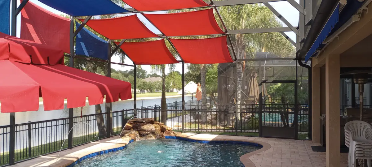 Red and blue shade sails over a pool and rock waterfall spa in a Florida pool cage