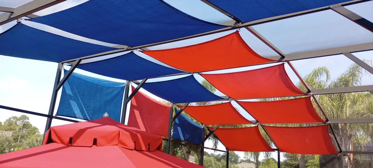 Red and blue shade sails over a pool cage with a red patio umbrella