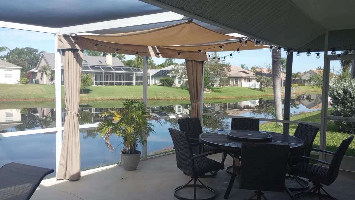 Tan shade sails over a lakefront lanai dining set with string lights