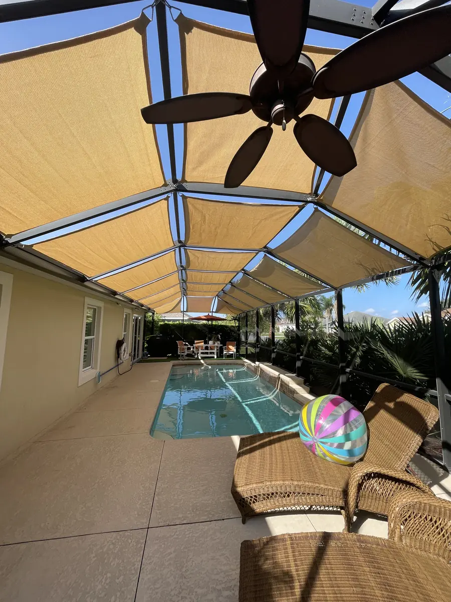 Tan shade sails over a lanai with a ceiling fan and a pool beyond