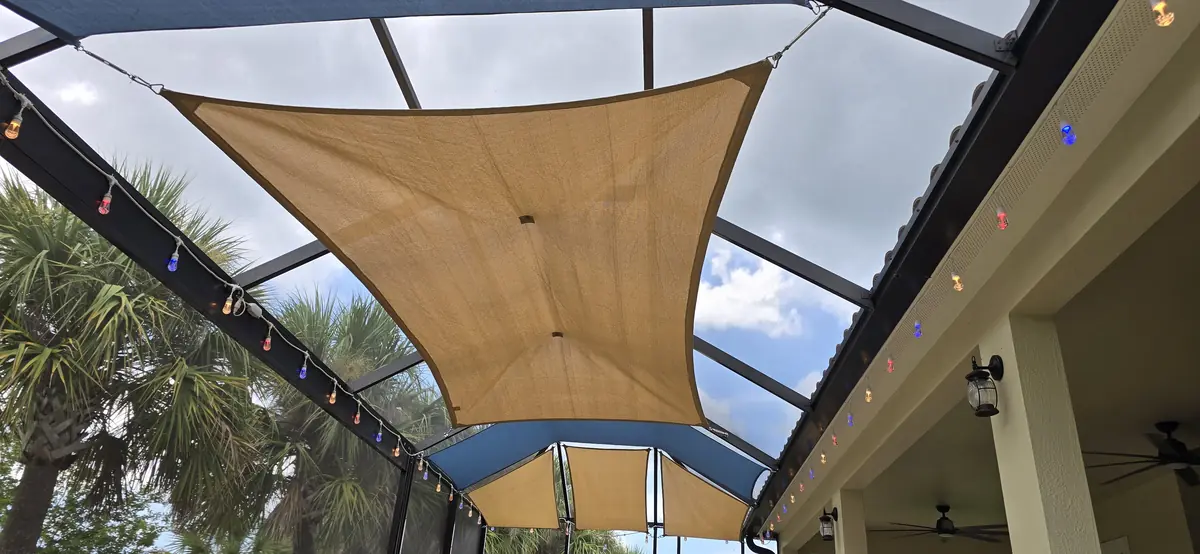Tan shade sail with string lights over a covered lanai and pool