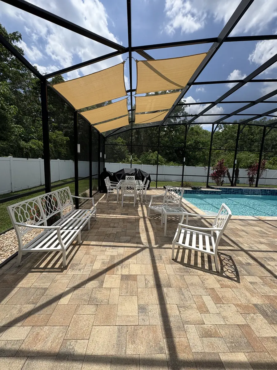Tan shade sail over a patio seating area beside a pool in a Florida screen enclosure