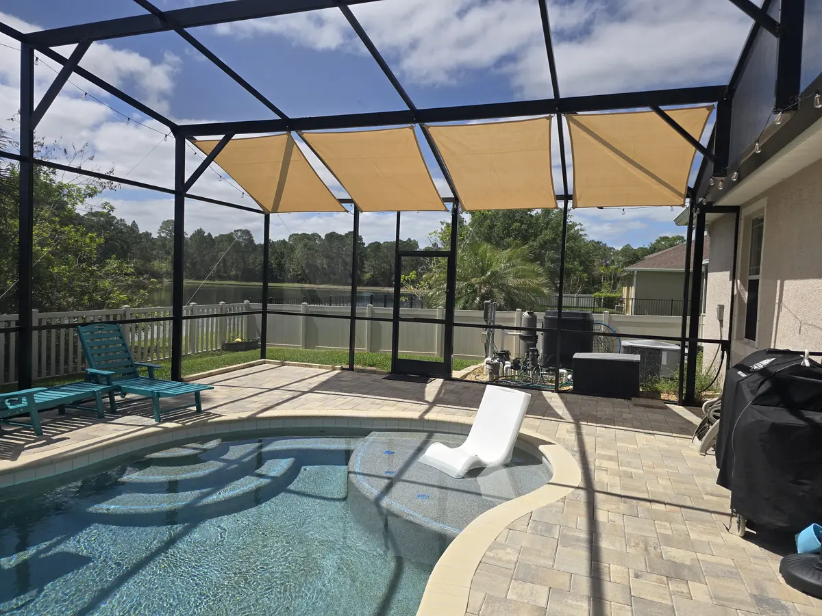 Tan shade sail over lounge chairs and a pool in a Florida lanai